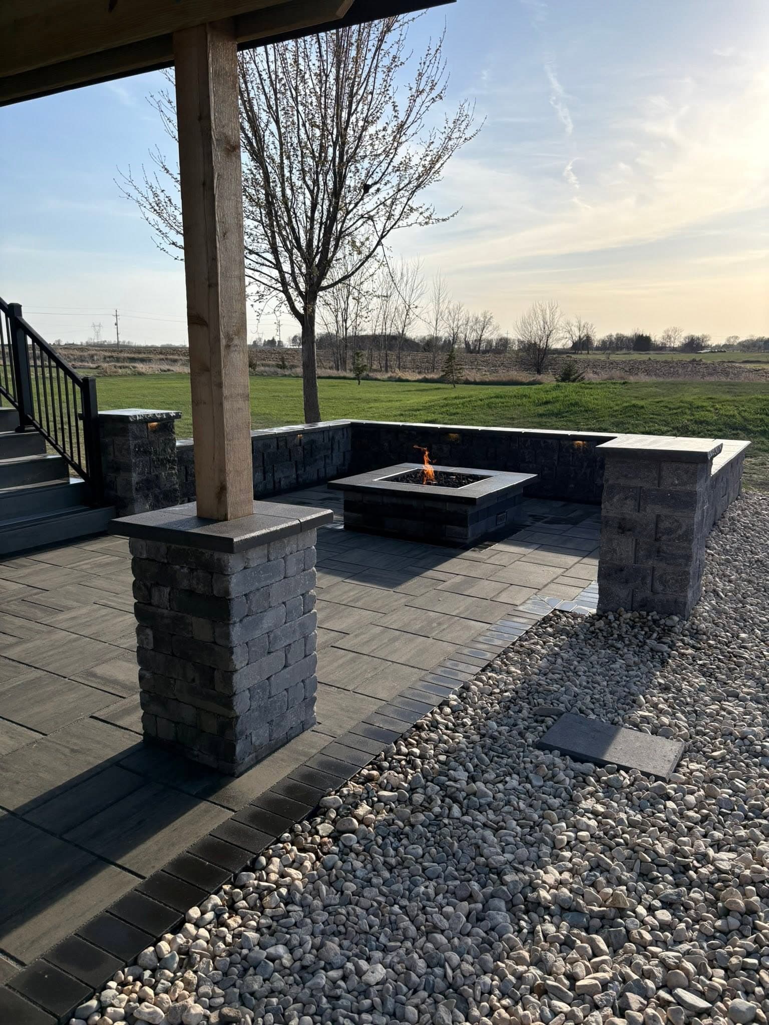 Fire table burning beside seat walls and a stone pillar, river rock in the foreground