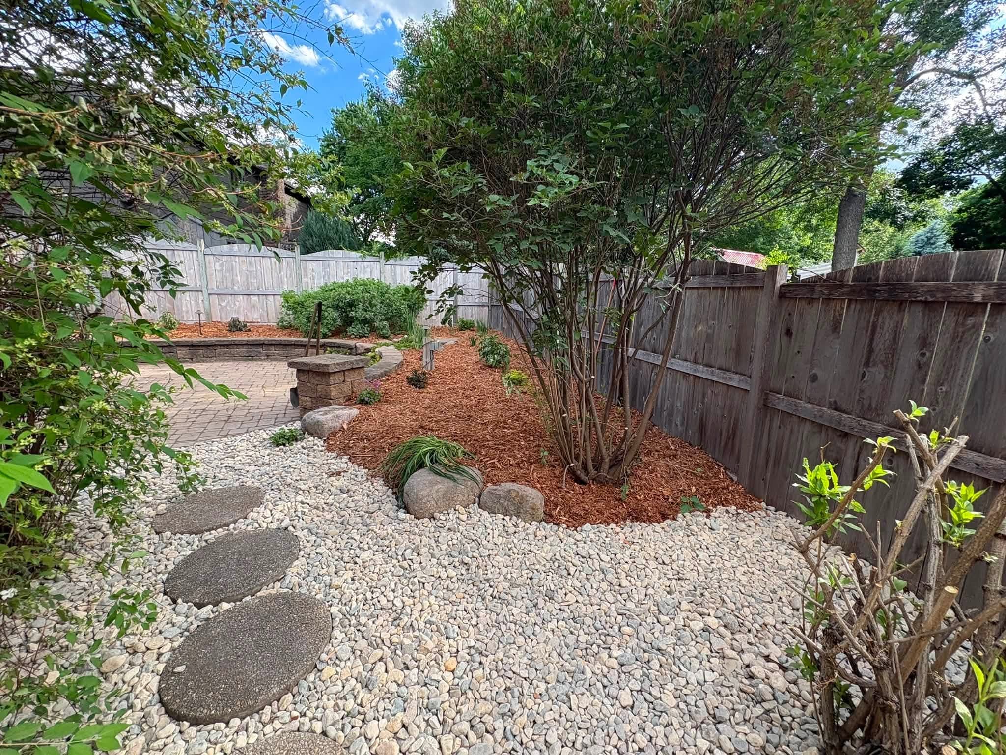 Stepping stones through river rock beside mulched planting beds