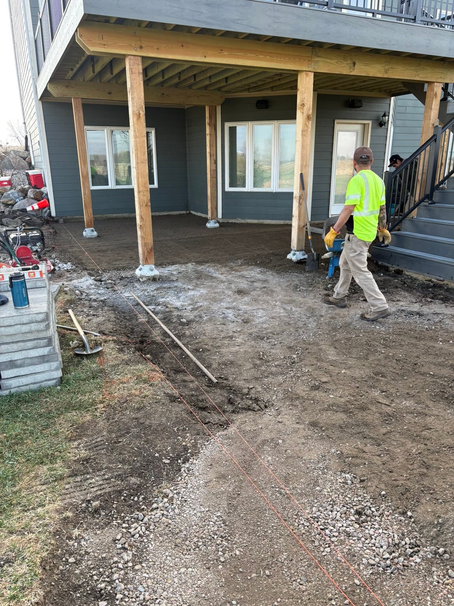 Crew prepping an under-deck patio base, string lines set