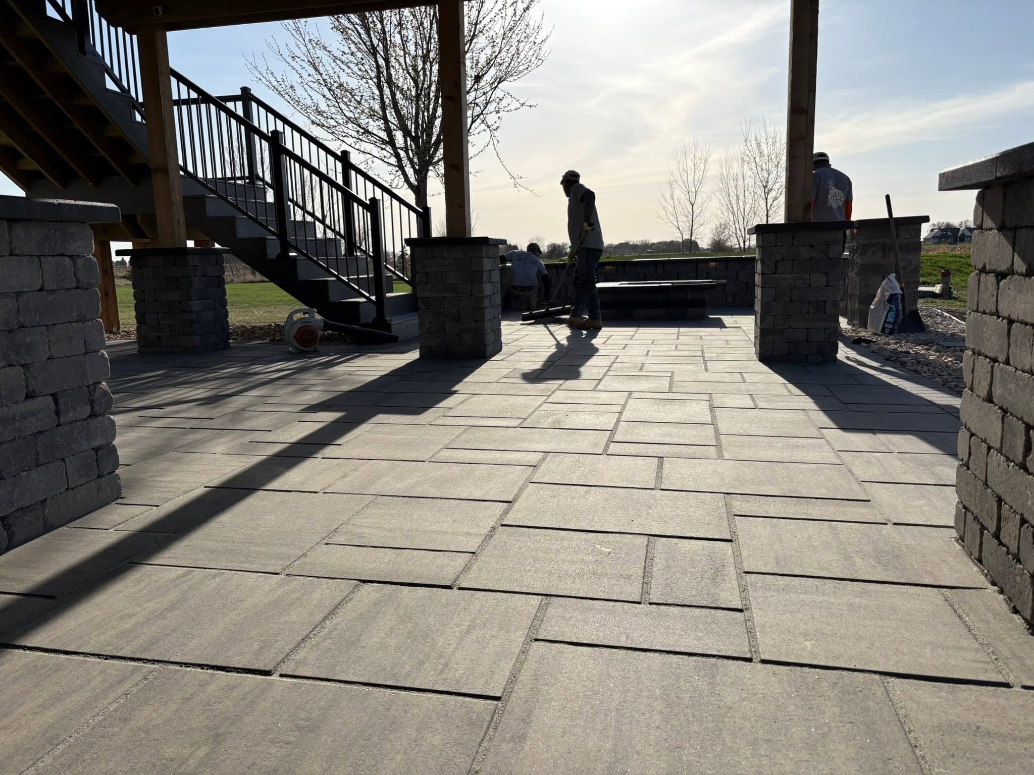 Crew finishing a paver patio under new pergola posts