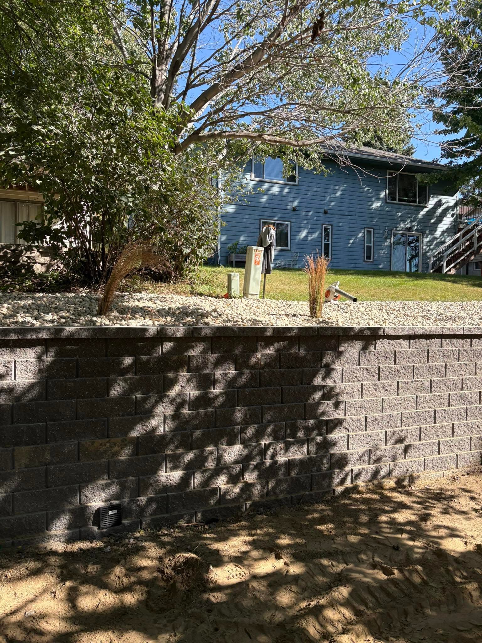 Block retaining wall standing, backfill and grading still underway below