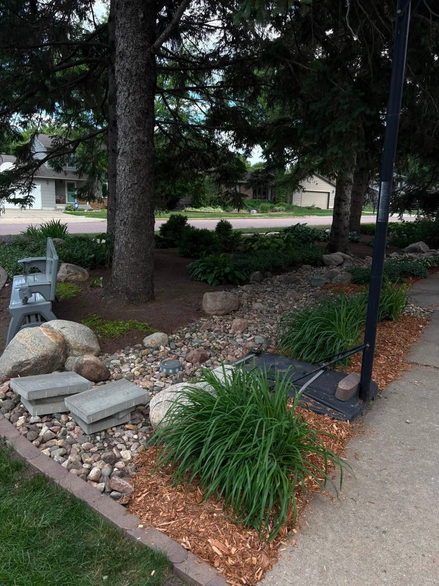 Corner bed with river rock, mulch, boulders, and a landscape light