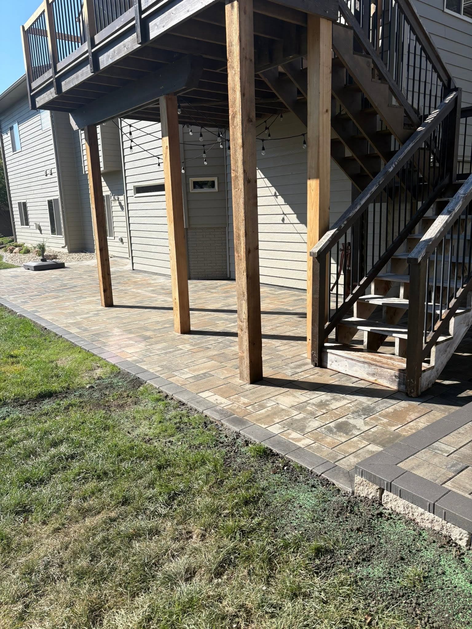 Paver patio built under the deck stairs, strung with cafe lights