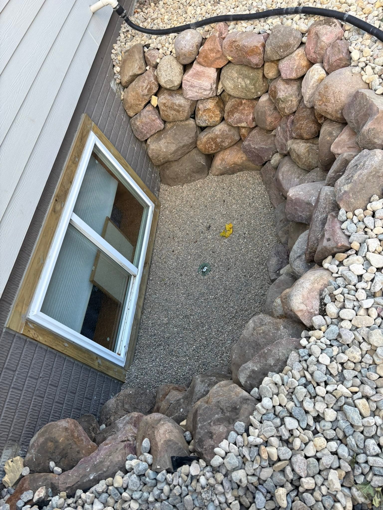 Boulder-walled window well finished with rock and a drain