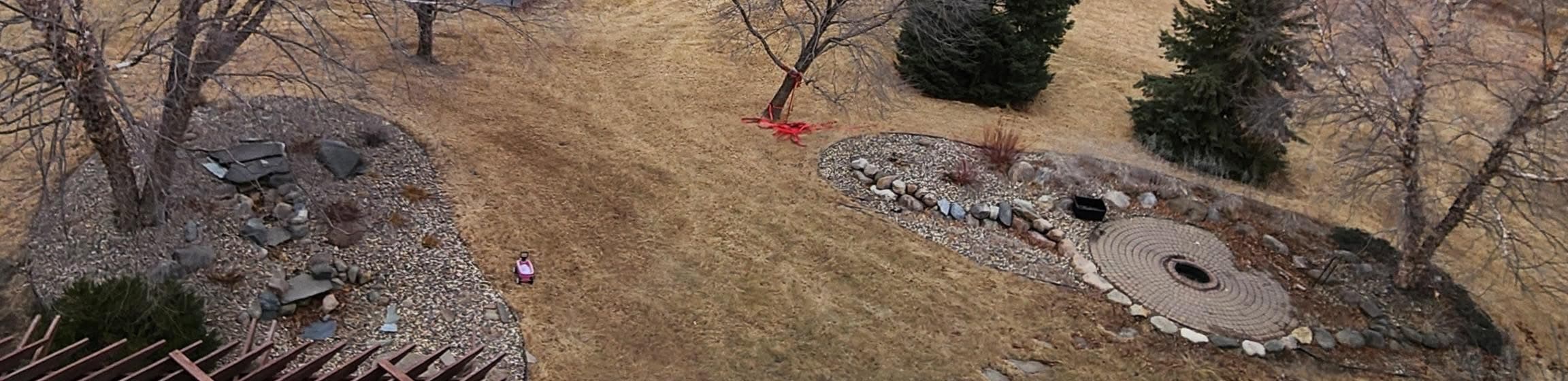 Wide panorama of a yard with rock beds, boulder features, and a circular paver ring