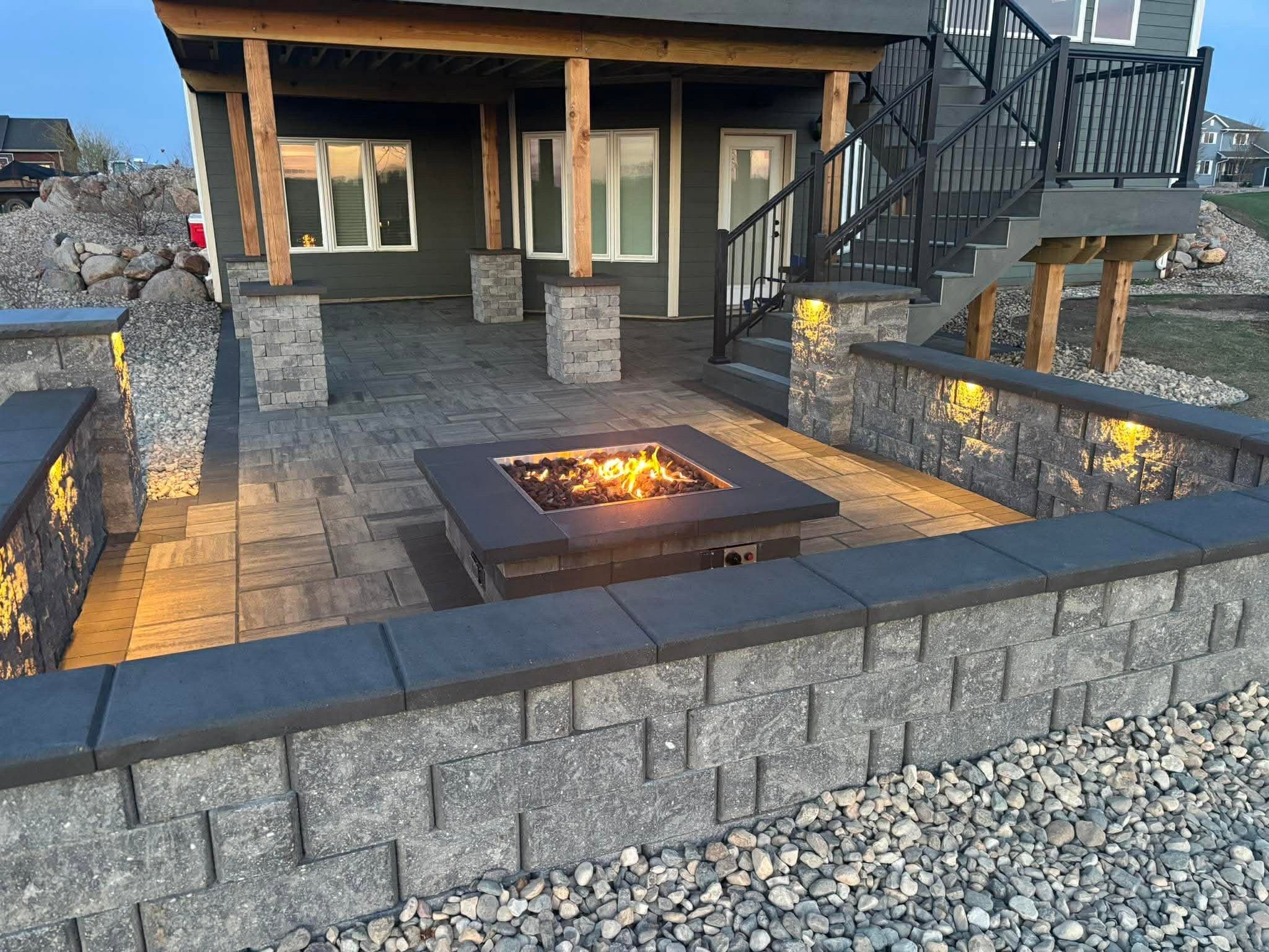 Square fire table burning at dusk on a walkout patio with lit seat walls