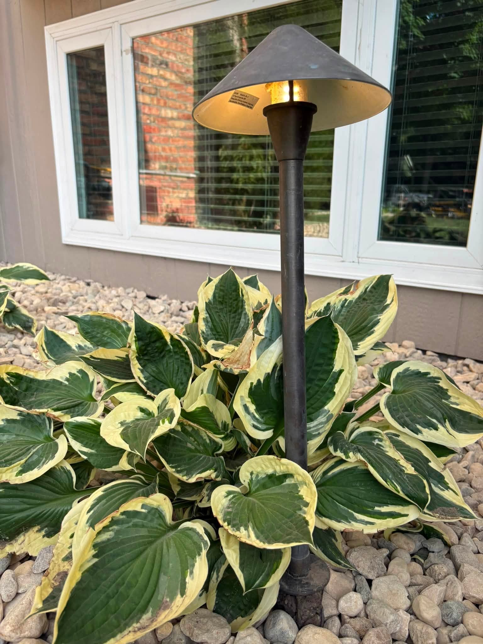 Landscape light glowing over hostas in a river rock bed