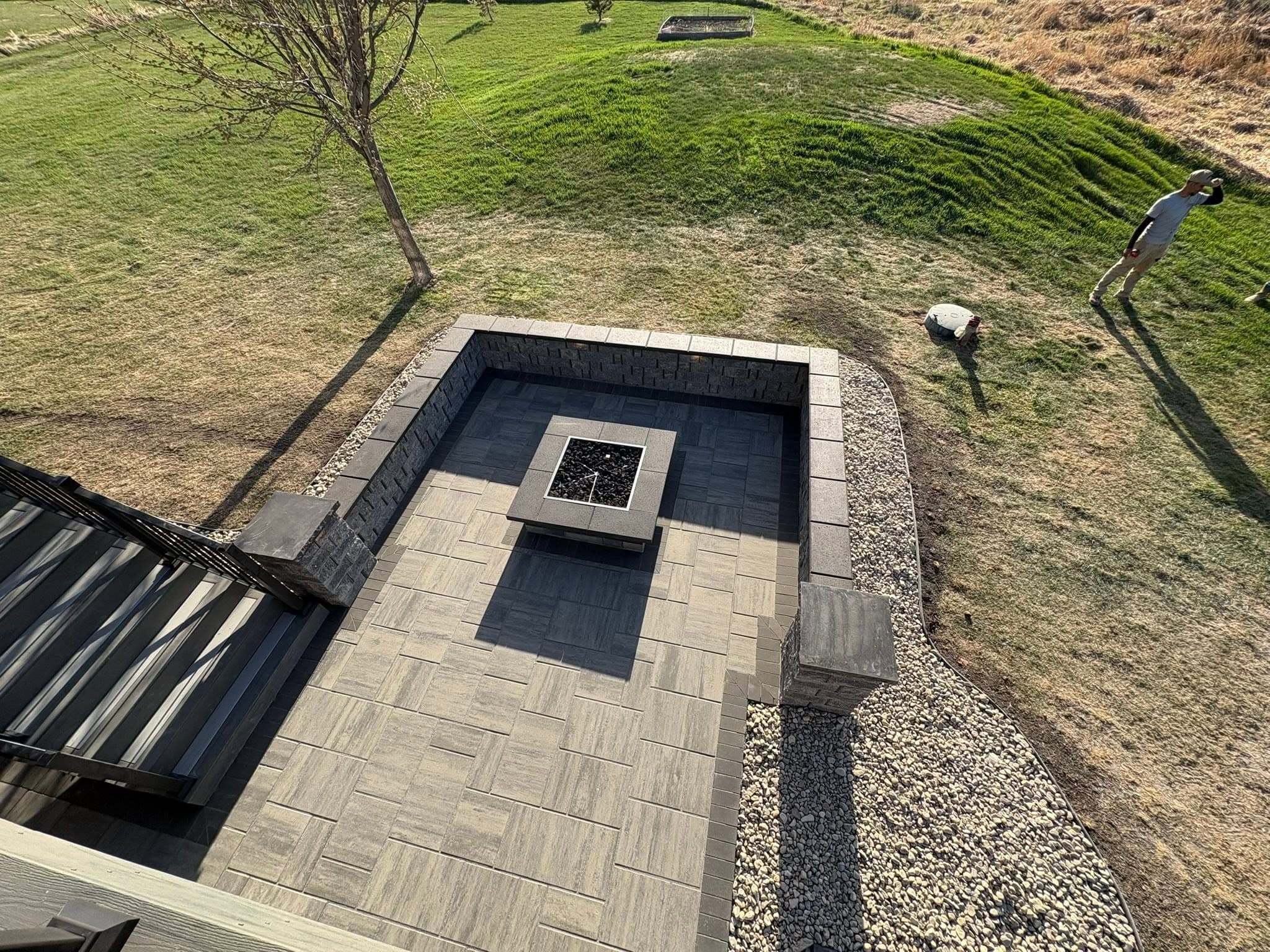 Finished sunken paver patio with seat walls and a fire table, seen from the deck above